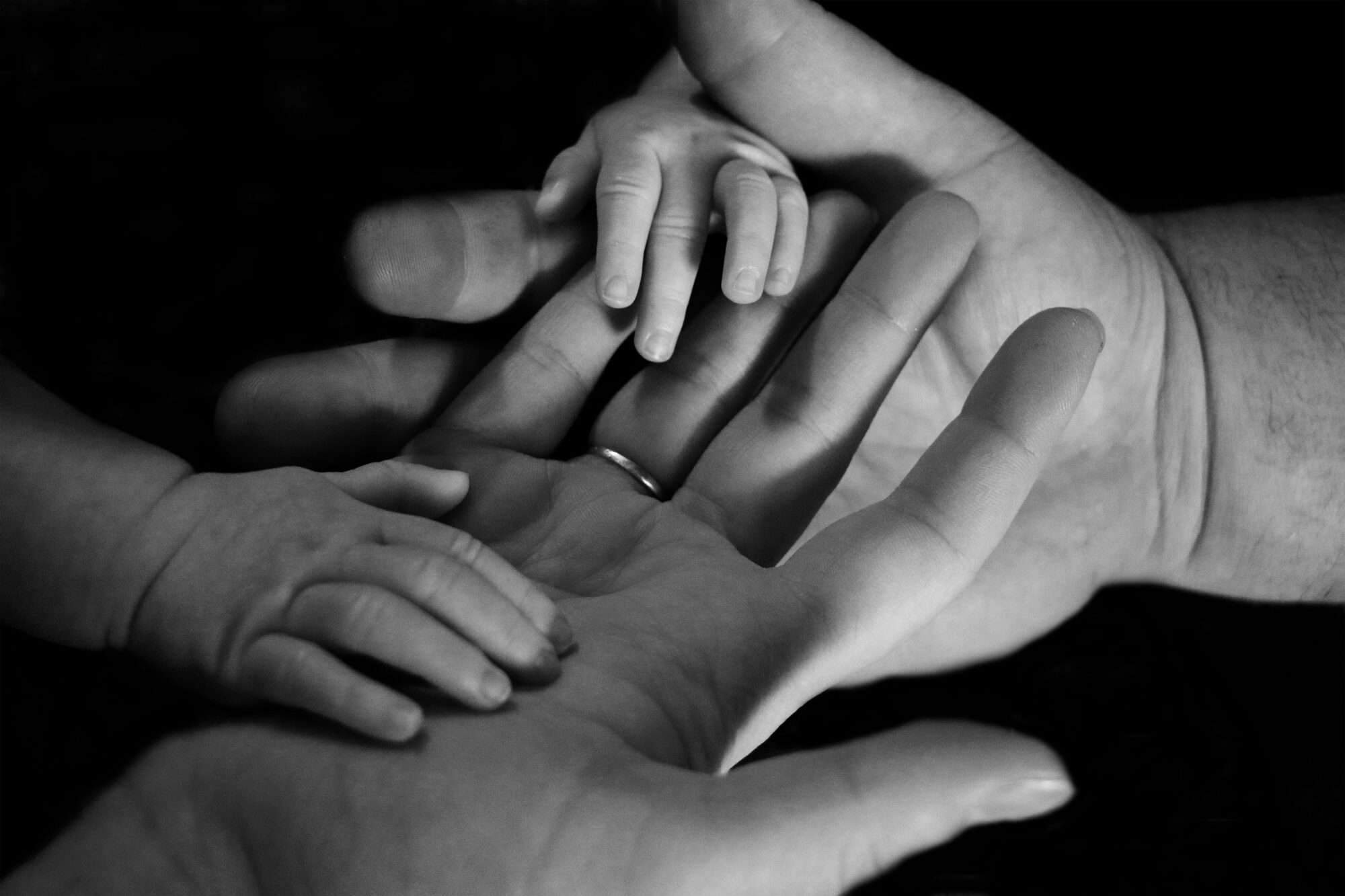A baby's hands resting in the open hands of two parents